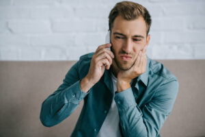 young man holding his jaw in pain whlie on the phone
