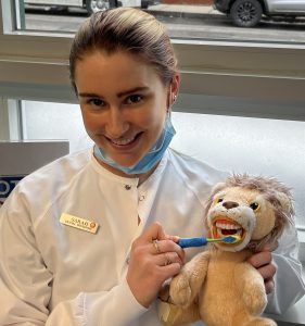 sarah smiling while brushing a stuffed lions teeth