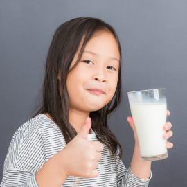 child holding a glass of milk and giving a thumbs up